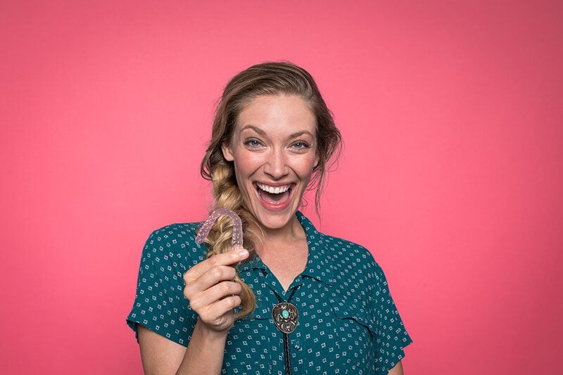 A woman smiling holding clear correct clear aligners