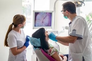 A dentist and assistant working on a patient using an intraoral camera in front of a screen